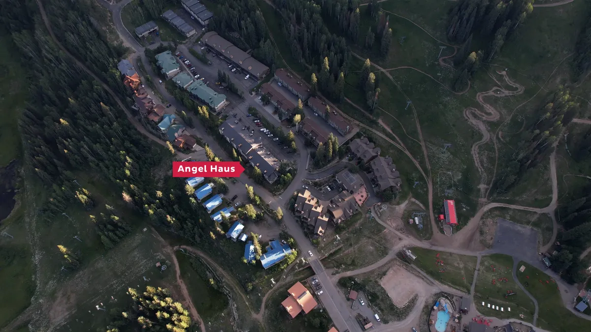 An exterior view featuring Angel Haus among other lodges, winding trails, and forested areas dusted with snow. The serene mood and visible trails highlight easy access to outdoor activities.
