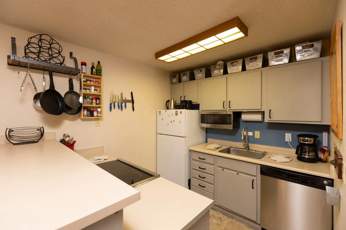 A functional kitchen scene with a countertop bar, bar seating, visible appliances, and hanging pots and utensils. The space feels lived-in yet tidy, ideal for family gatherings and shared meal preparation.