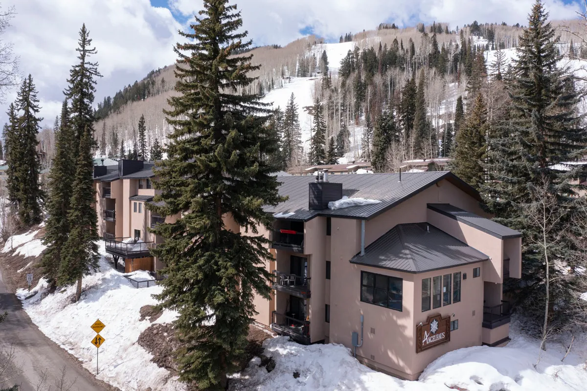 A snowy exterior shot of the Angel Haus building surrounded by trees, with a clear view of the mountain backdrop. The snow-covered ground and inviting architecture convey proximity to both the slopes and the tranquility of the mountain environment.